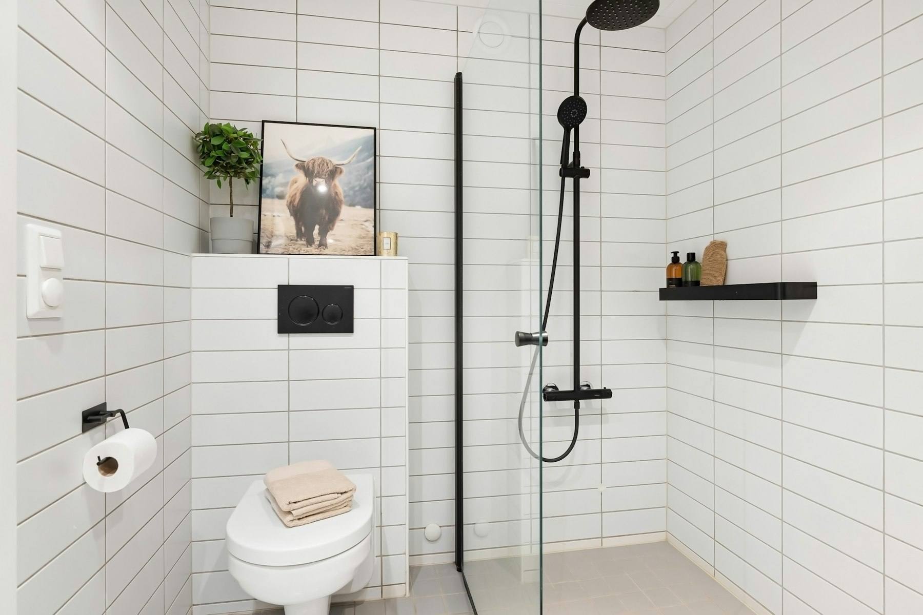Lille badeværelse med hvide fliser, væghængt toilet og bruser