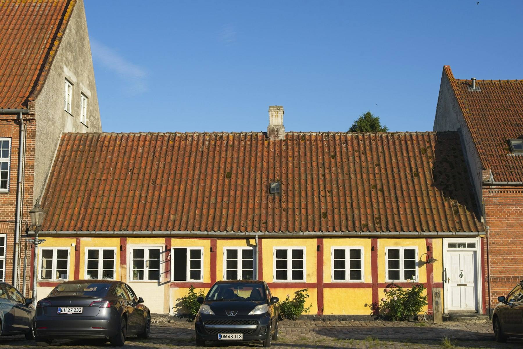 Gult dansk hus med rødt tegltag og biler foran